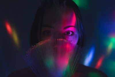 Close-up portrait of young woman holding illuminated fiber optic in darkroom