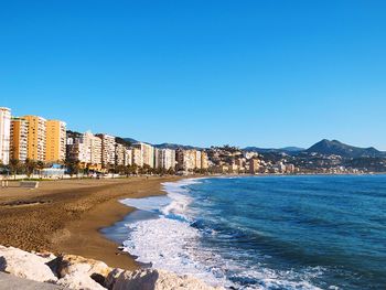 Buildings by sea against clear blue sky