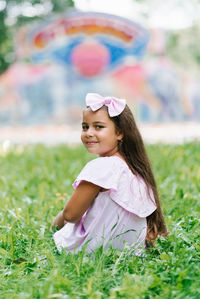 A cute little girl in the park is sitting on the grass and smiling