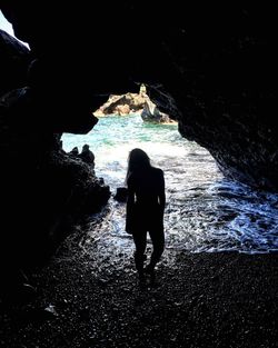 Rear view of silhouette woman standing on rock at beach