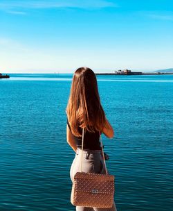 Rear view of woman standing by sea against sky