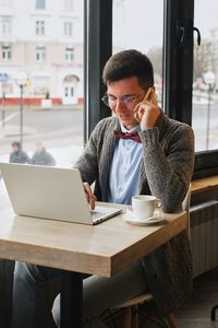 Young man using phone while sitting on table