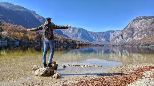 Rear view of man standing on rock by lake against sky