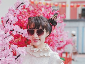 Portrait of smiling woman in sunglasses by pink flowers