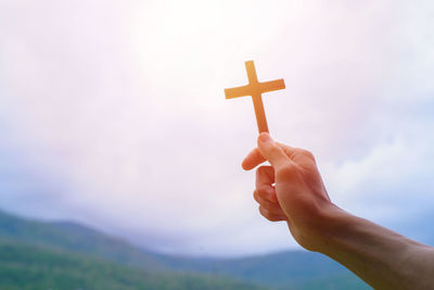 Midsection of person holding cross against sky