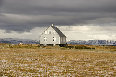 Small house with corrugated metal facade on a concrete basement in a partly snow-covered field