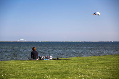 People sitting on land by sea against clear sky