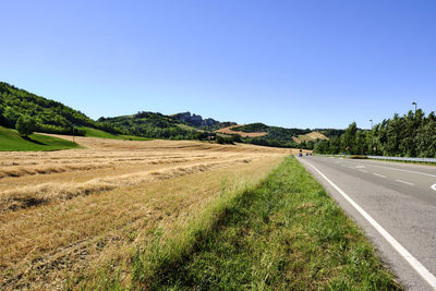 Empty road amidst field against clear blue sky