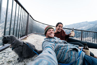 Young couple enjoys a time in wilderness taking selfies laughing and having fun with their gray cat