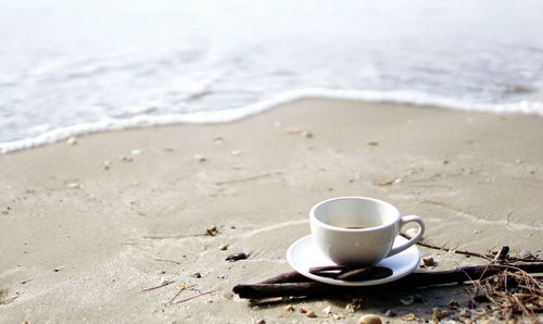 Close-up of coffee cup on shore at beach