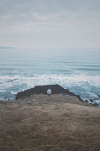 Rear view of man walking on rock against sea and sky