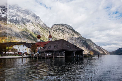 Built structure by lake and buildings against sky