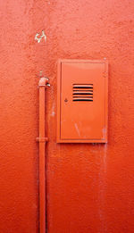 Vertical metal pipe and electric box on orange color wall in burano, venice, italy