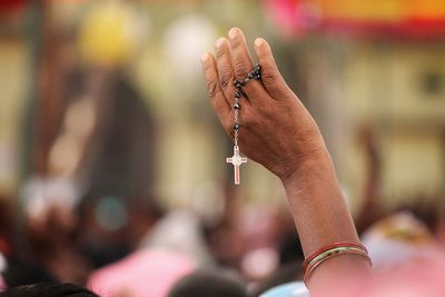 Close-up of woman holding rosary in hand against blurred background