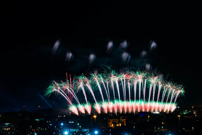 Firework display over city against sky at night