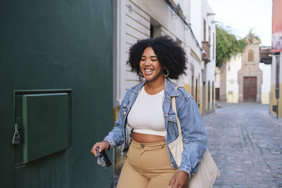 Happy young woman with camera walking in alley