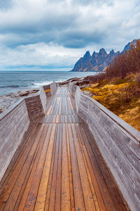 Empty boardwalk by sea against cloudy sky