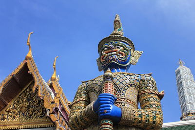 Low angle view of monster statue and temple against blue sky