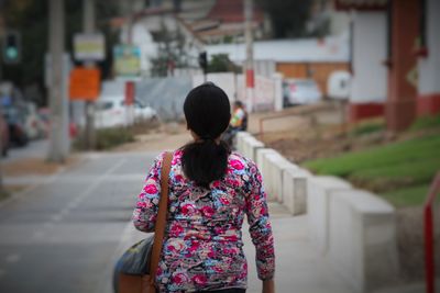 Rear view of woman walking on sidewalk in city