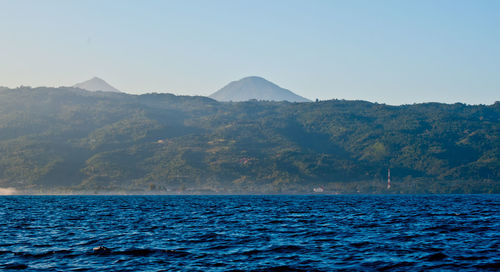 Scenic view of sea by mountain against clear sky