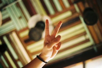 Cropped hand of person gesturing peace sign against ceiling at home