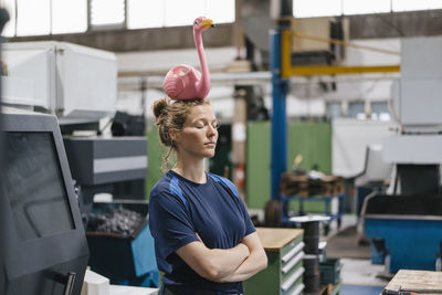 Young woman working as a skilled worker in a high tech company, balancing a pink flamingo on her head