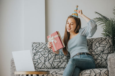 Young woman holding gift sitting on sofa at home