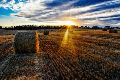 Hay bales at farm against cloudy sky during sunrise