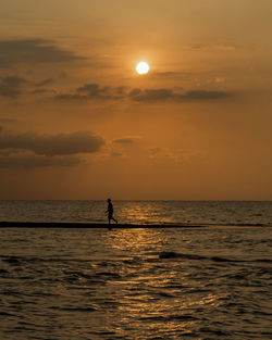 Silhouette man on sandbar against sky during sunset