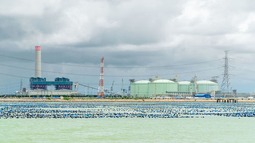 View of factory by sea against sky