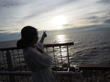 Rear view of man standing on railing against sea