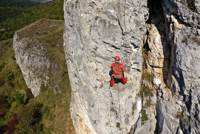 Aerial view of mountain rescuer abseiling on a rocky wall hanging on a rope