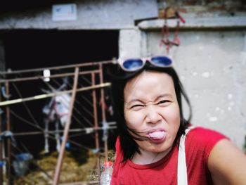 Portrait of young woman sticking out tongue while standing against wall