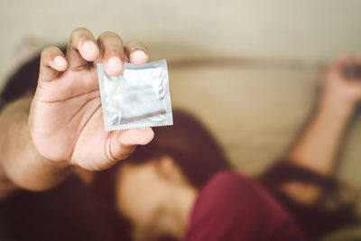 Close-up up couple holding condom lying on bed at home