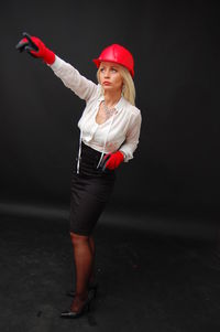 Businesswoman wearing red hardhat while pointing against black background