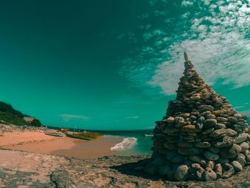 Stacked pebbles at beach against cloudy sky