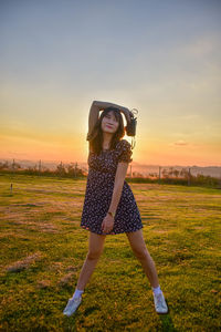 Portrait of young woman standing on field against sky during sunset