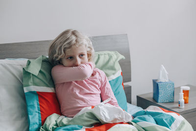 Sick ill girl with fever lying in bed at home with flu, fever. child coughing sneezing in elbow