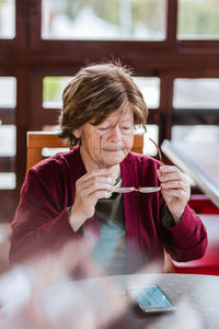 High angle of senior woman in glasses sitting at table and browsing social media on smartphone at home
