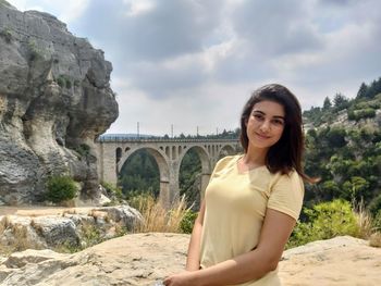 Portrait of smiling young woman standing against arch bridge