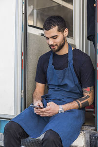 Young male entrepreneur text messaging while sitting at entrance of food truck