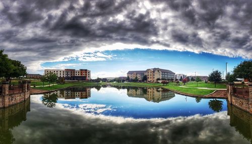 Reflection of buildings in lake against cloudy sky