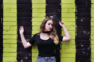 Portrait of young woman standing against yellow wall