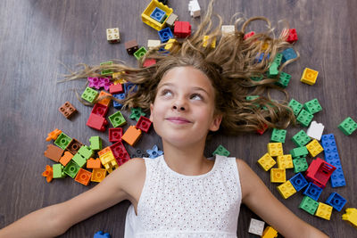 High angle view of smiling girl with toy blocks lying on floor