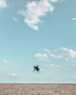 Surface level shot of man jumping on beach against sky