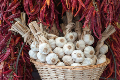 Close-up of garlic cloves in wicker basket amidst dried red chili peppers at market stall