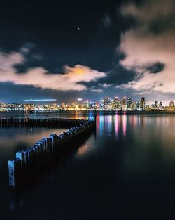 Groyne in river by illuminated city at night