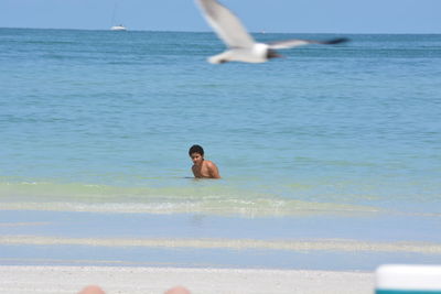 Full length of shirtless man in sea against sky