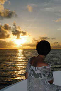 Rear view of woman looking at sea against sunset sky