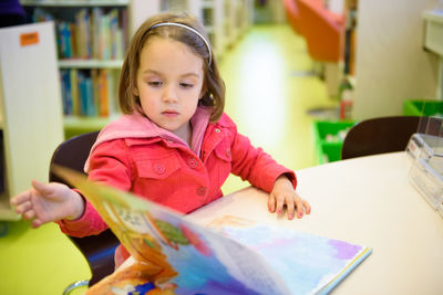 Girl reading book while sitting on chair in library